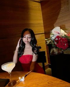 a woman sitting at a table with a martini in front of her and flowers behind her