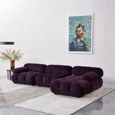 a large purple couch sitting on top of a white rug in a living room next to a painting