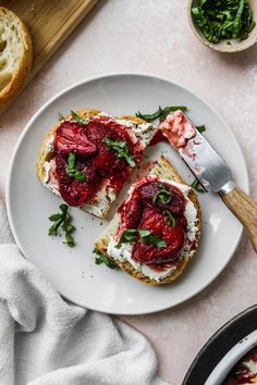 two pieces of bread with cream cheese and strawberries on them next to a knife