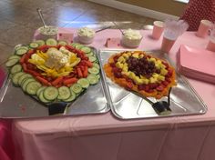 two trays filled with different types of food on top of a pink table cloth