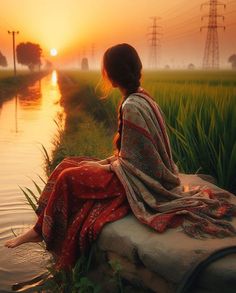 a woman sitting on top of a rock next to a body of water at sunset