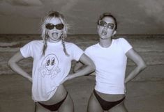 two young women in bathing suits standing on the beach with their hands on their hips