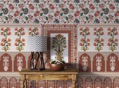 a table with a lamp on top of it next to a flowered wallpaper