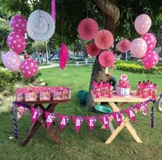 a table with pink and purple decorations on it in the grass next to a tree