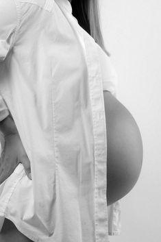 a pregnant woman is holding her stomach up to the side while wearing a white shirt