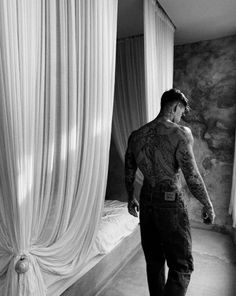 a man with tattoos standing in front of a bed