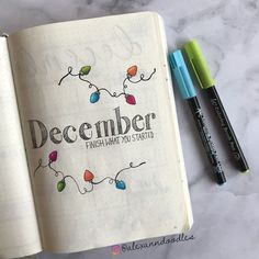 an open notebook with the words december written on it next to two markers and a pen