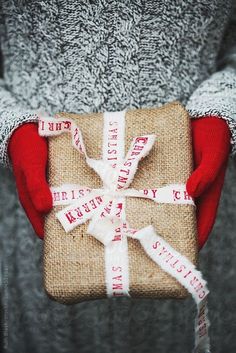 a person holding a wrapped present with white ribbon and red mittens on their hands