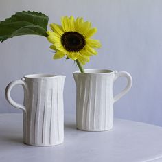 two white vases with a yellow sunflower in them