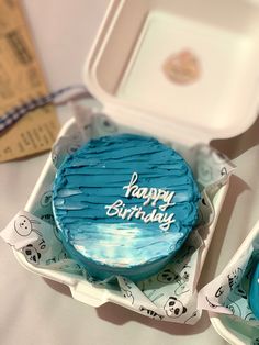 a blue birthday cake sitting on top of a white plate next to a plastic container