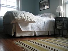 a white bed sitting in a bedroom on top of a hard wood floor next to a window