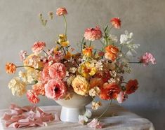 a vase filled with lots of different colored flowers on top of a white tablecloth