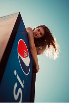 a woman leaning on the side of a pepsi sign with her hair blowing in the wind