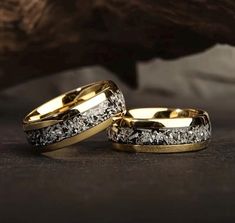 two gold wedding bands with white diamonds on them sitting next to each other in front of a rock