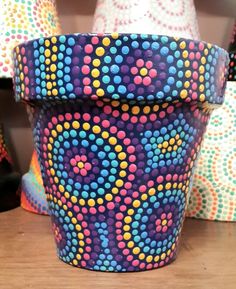 a colorful flower pot sitting on top of a wooden table next to other vases