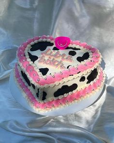 a heart shaped cake with pink and white frosting on top sitting on a silver cloth