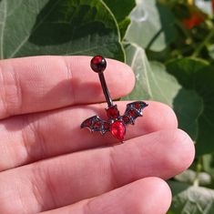 a person is holding a tiny red jeweled bat navel ring in their left hand