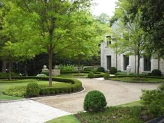 a stone house surrounded by lush green trees and shrubbery on either side of the driveway