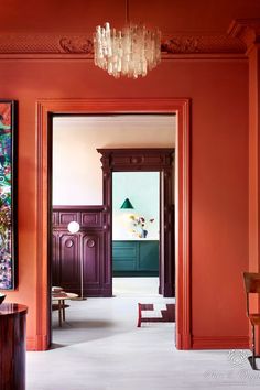 an orange room with red walls and paintings on the wall, along with a wooden table