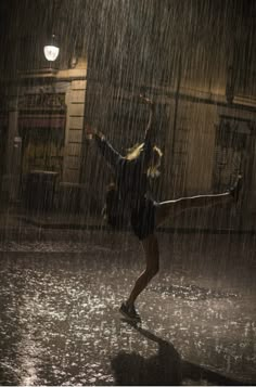 a woman dancing in the rain at night with her arms up and legs spread out