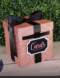 a pink gift box with a black ribbon and name card on it sitting on a wooden table