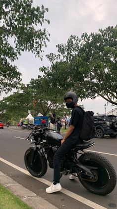 a man riding on the back of a motorcycle down a street next to a park