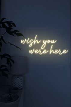 a neon sign that says wish you were here on the wall next to a potted plant