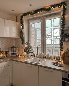 a kitchen decorated for christmas with lights and garland on the window sill over the sink