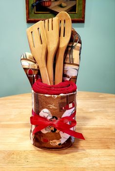 a wooden utensil holder filled with kitchen utensils and cloth wrapped in red ribbon