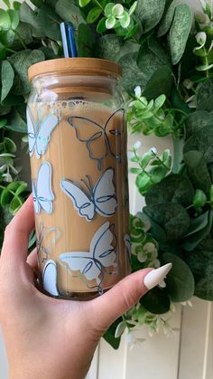 a hand holding a cup with a straw in it and butterflies on the lid, next to a green wreath