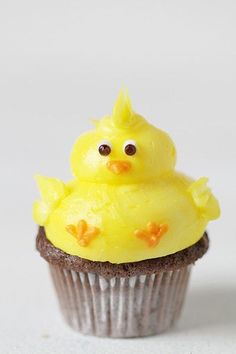 a cupcake with yellow frosting and a little bird on top, sitting in front of a white background