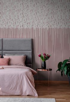 a bed with pink sheets and pillows next to a plant