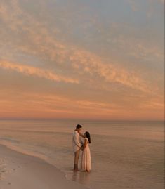 a man and woman standing on the beach at sunset