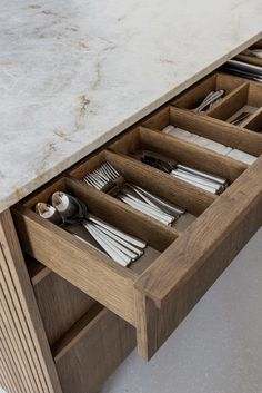 an open drawer with utensils and silverware in it on a marble counter top