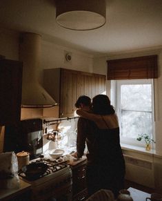 two people standing in a kitchen next to a window