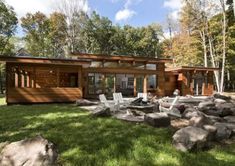 a house in the woods surrounded by rocks and trees with chairs on the grass near it