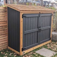 an outdoor storage shed with the doors open in front of a wooden fence and yard