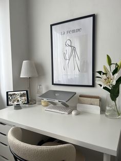 a white desk topped with a laptop computer next to a vase filled with flowers and a lamp