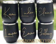 six black tumblers with gold writing on them sitting in front of a grass field