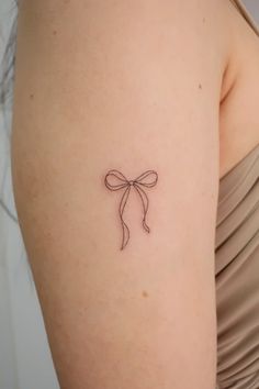 a small bow tattoo on the back of a woman's left upper arm,