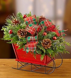 a christmas sleigh with red roses and greenery in it on a table