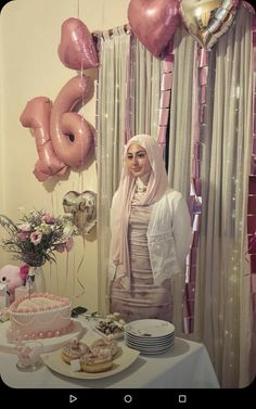 a woman standing in front of a table with pink balloons and cake on top of it