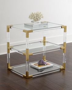 a glass table with gold trimmings and a white flower on top, sitting on a wooden floor