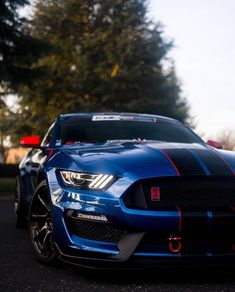 a blue mustang with red stripes parked on the side of a road next to trees