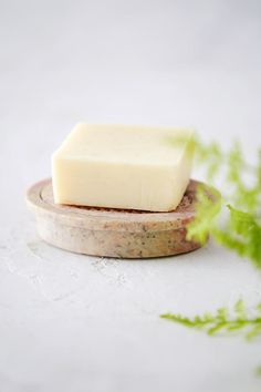 a bar of soap sitting on top of a wooden plate next to a plant with green leaves