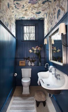 a bathroom with blue walls and floral wallpaper on the ceiling, along with a white toilet and sink