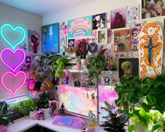 a desk with a computer and lots of plants on it in front of a wall full of posters