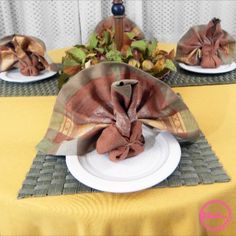 two plates with napkins on them are sitting on a yellow cloth covered tablecloth