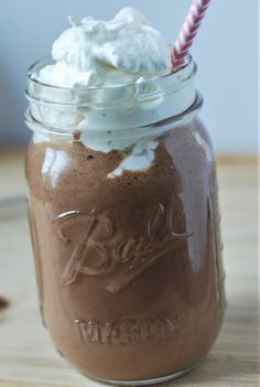 a chocolate drink with whipped cream and a striped straw in a mason jar on a wooden table