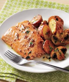 a white plate topped with salmon and potatoes next to a fork on a green napkin